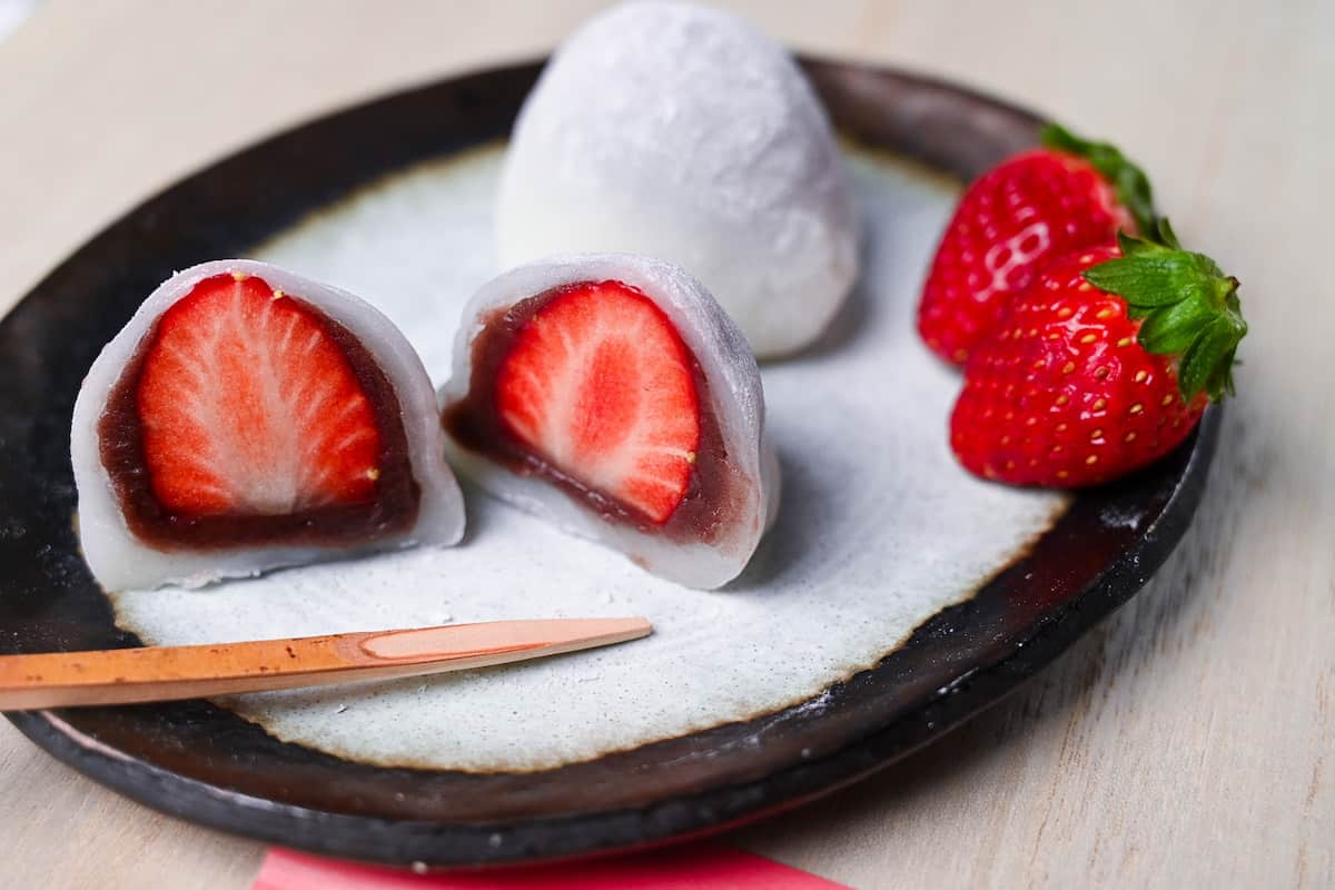 Homemade ichigo daifuku (strawberry mochi) cut in half and served on a plate with strawberries