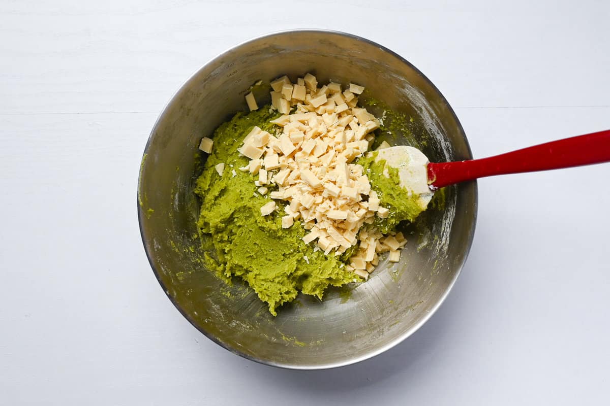 Adding white chocolate chunks to matcha cookie dough in a mixing bowl