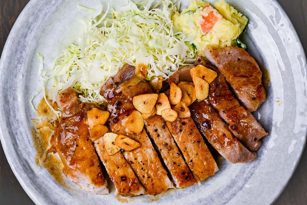 Tonteki Japanese pork steak served with fried garlic chips, shredded cabbage and potato salad top down