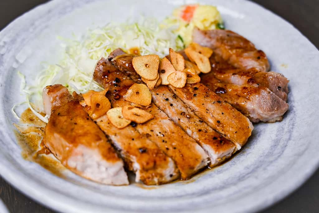 Tonteki Japanese pork steak served with fried garlic chips, shredded cabbage and potato salad side view