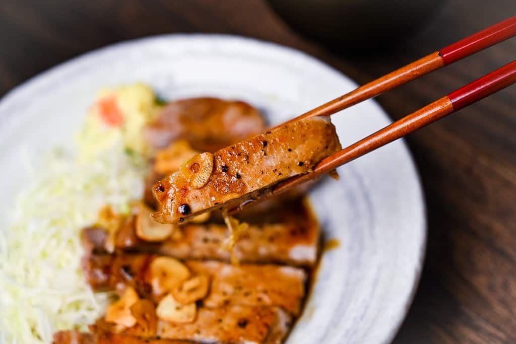 A piece of tonteki pork steak held with wooden chopsticks