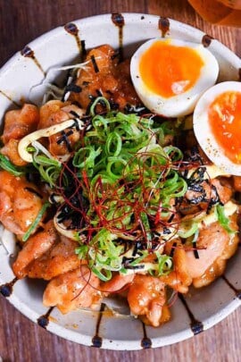 Teriyaki Chicken Donburi topped with chopped green onion, kizami nori, mayo and soft boiled eggs in a cream and brown stripy bowl