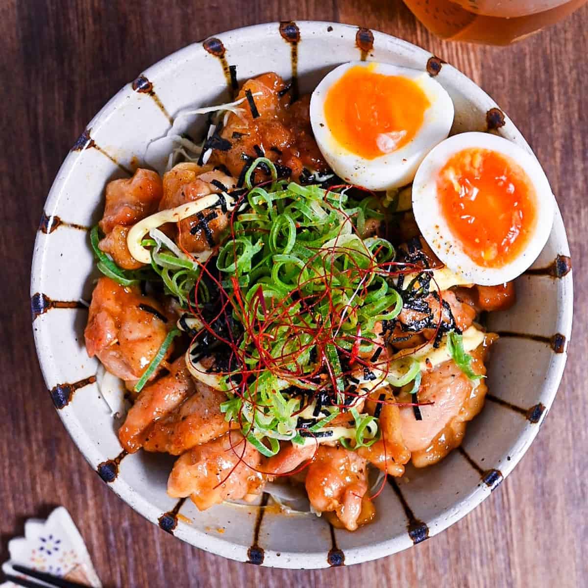 Teriyaki Chicken Donburi topped with chopped green onion, kizami nori, mayo and soft boiled eggs in a cream and brown stripy bowl