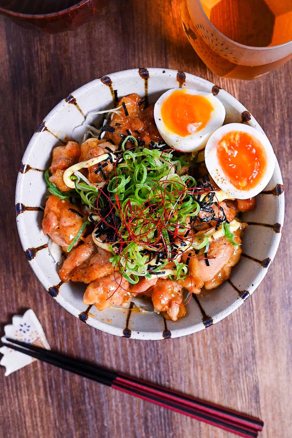 Teriyaki Chicken Donburi topped with chopped green onion, kizami nori, mayo and soft boiled eggs in a cream and brown stripy bowl