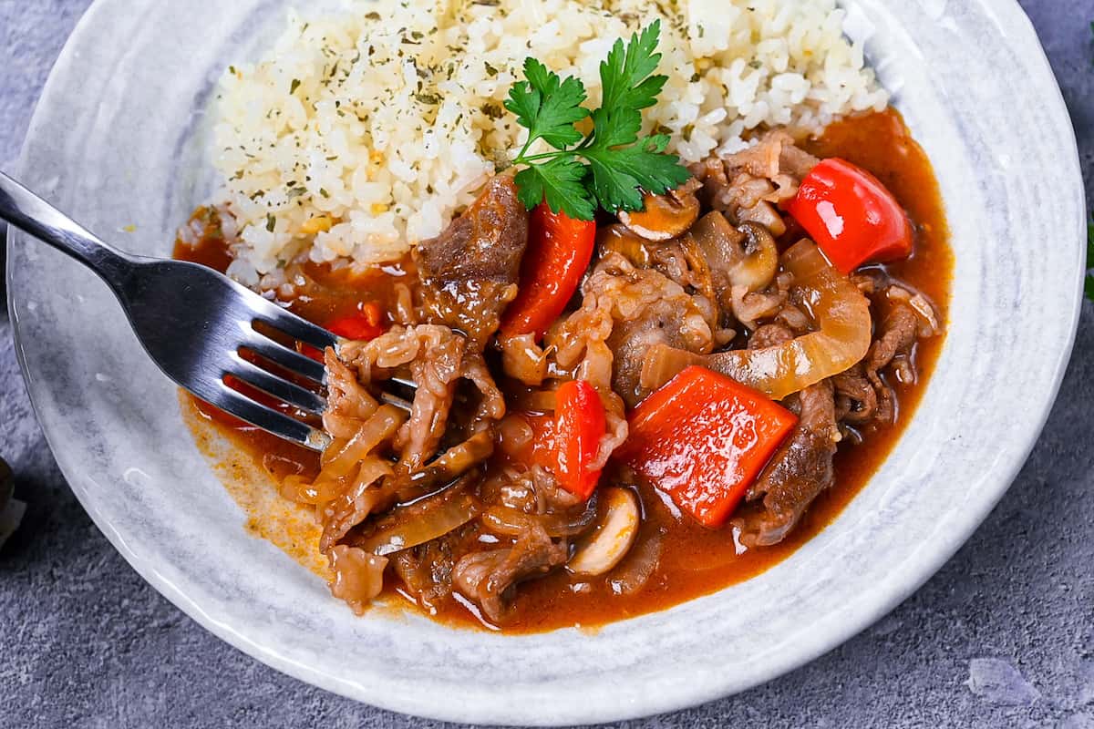 Japanese beef hayashi rice with garlic butter rice topped with fresh parsley close up with fork