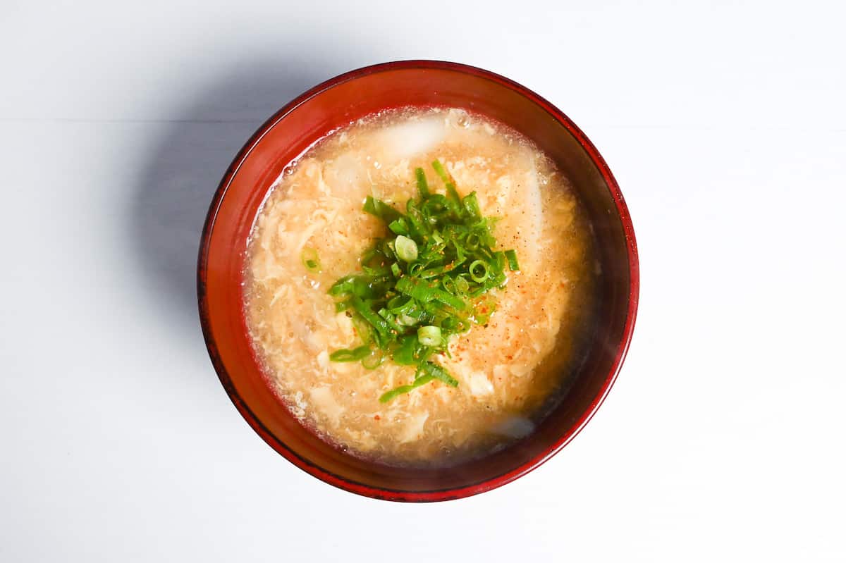 Japanese egg drop soup in a red bowl topped with chopped green onion and shichimi togarashi
