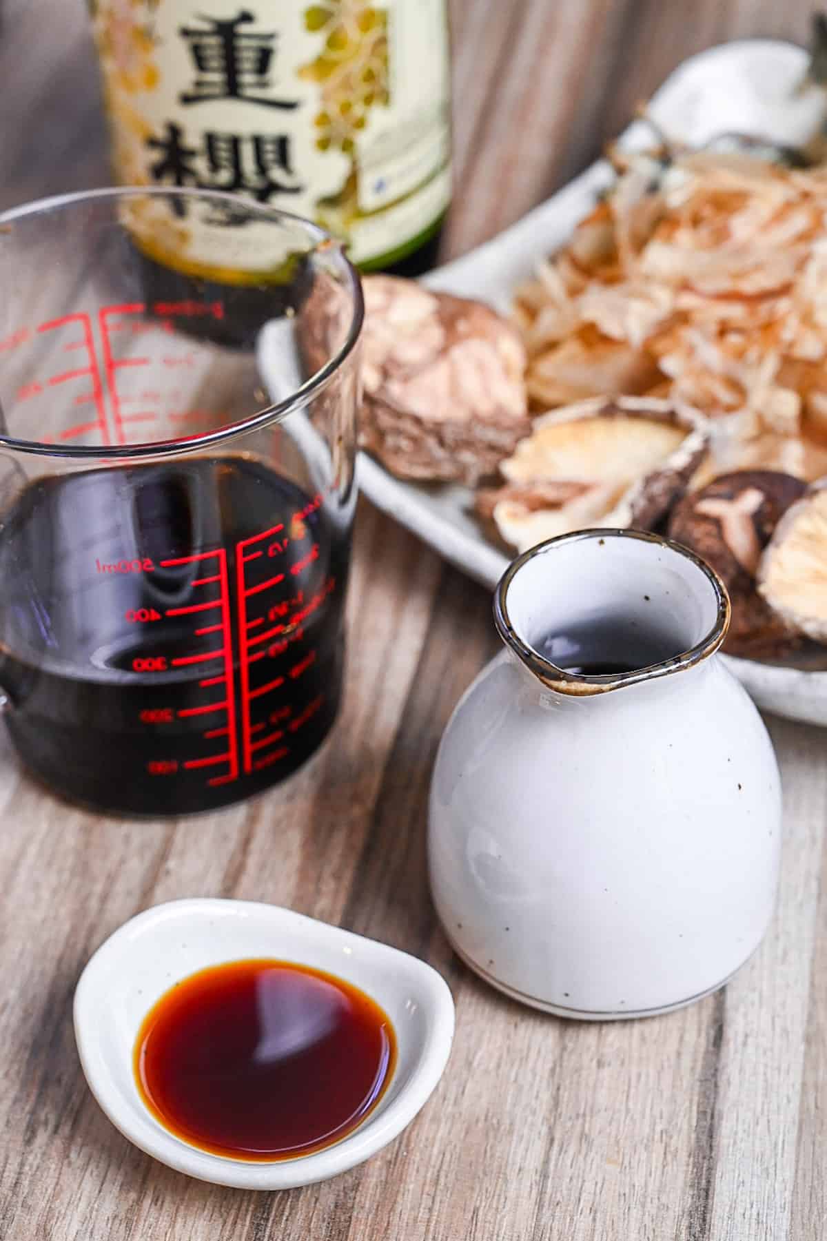 tsuyu sauce in white ceramic bottle and dipping dish next to a plate of shiitake, kombu and bonito flakes (dashi ingredients)