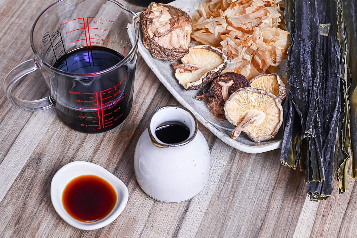 tsuyu sauce in white ceramic bottle and dipping dish next to a plate of shiitake, kombu and bonito flakes (dashi ingredients)