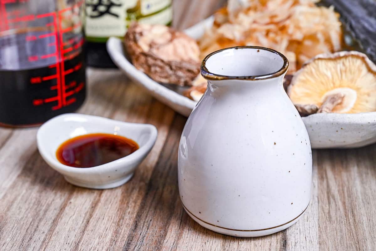 tsuyu sauce in white ceramic bottle and dipping dish next to a plate of shiitake, kombu and bonito flakes (dashi ingredients)