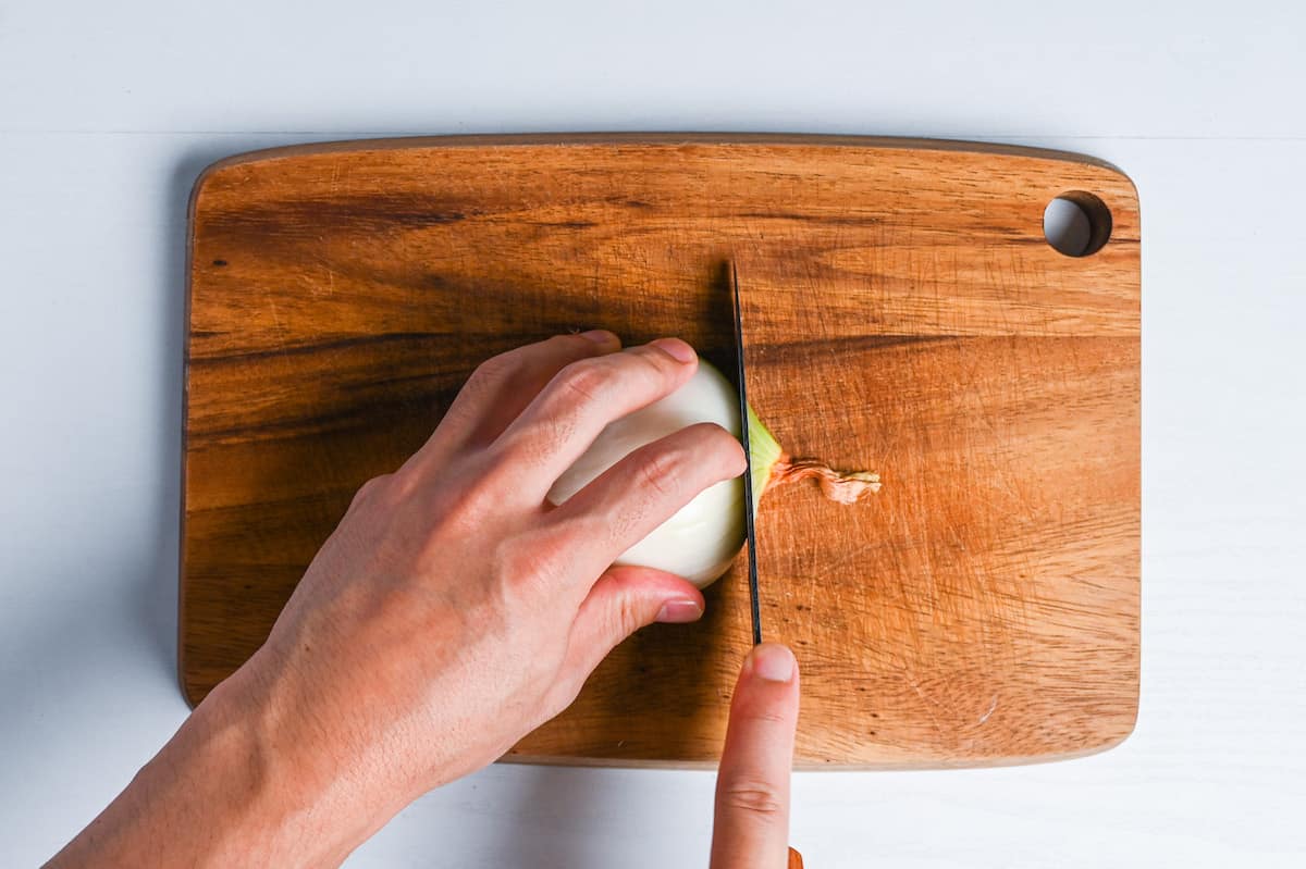 cutting one end off of half an onion on wooden chopping board