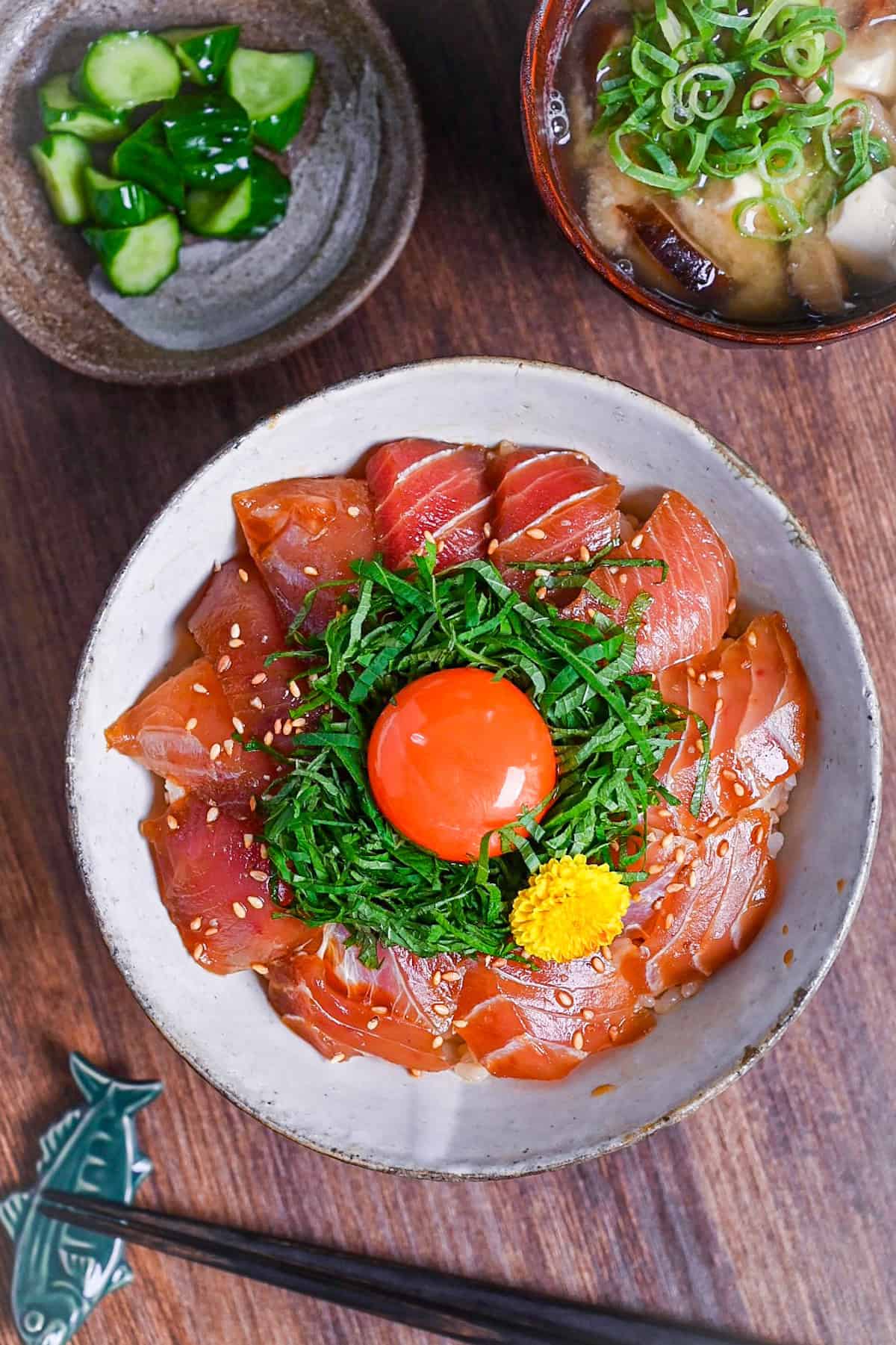 maguro zuke don (marinated tuna sashimi bowl) topped with shredded shisho, raw egg yolk and yellow flower next to pickles and miso soup