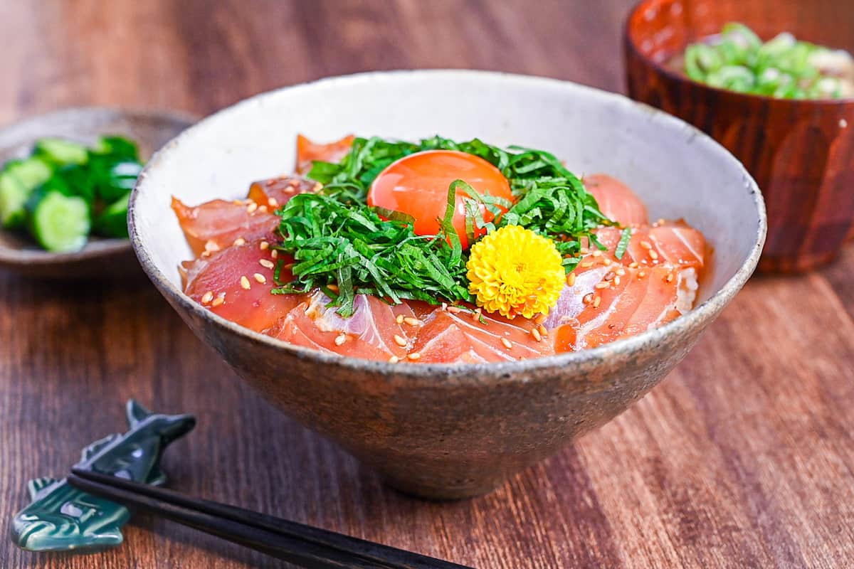 maguro zuke don (marinated tuna sashimi bowl) topped with shredded shisho, raw egg yolk and yellow flower next to pickles and miso soup