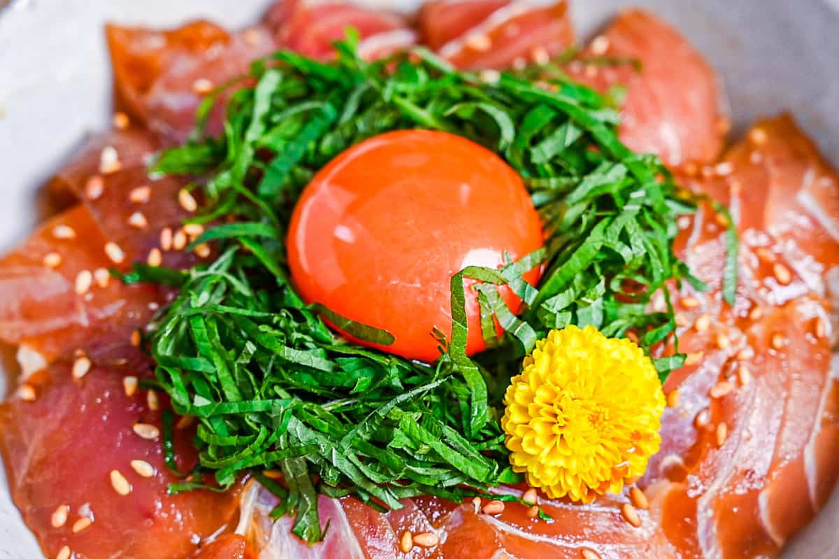 maguro zuke don (marinated tuna sashimi bowl) topped with shredded shisho, raw egg yolk and yellow flower close up