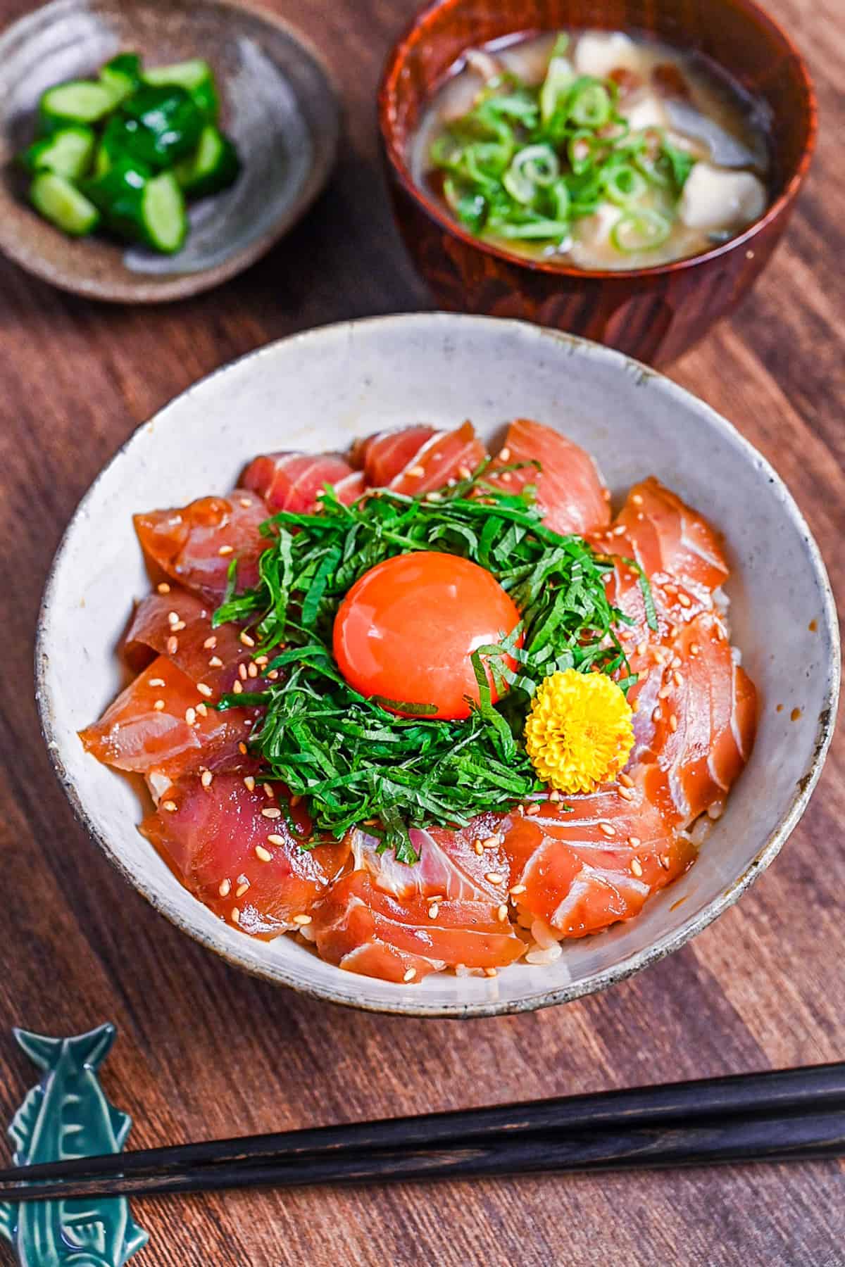 maguro zuke don (marinated tuna sashimi bowl) topped with shredded shisho, raw egg yolk and yellow flower next to pickles and miso soup