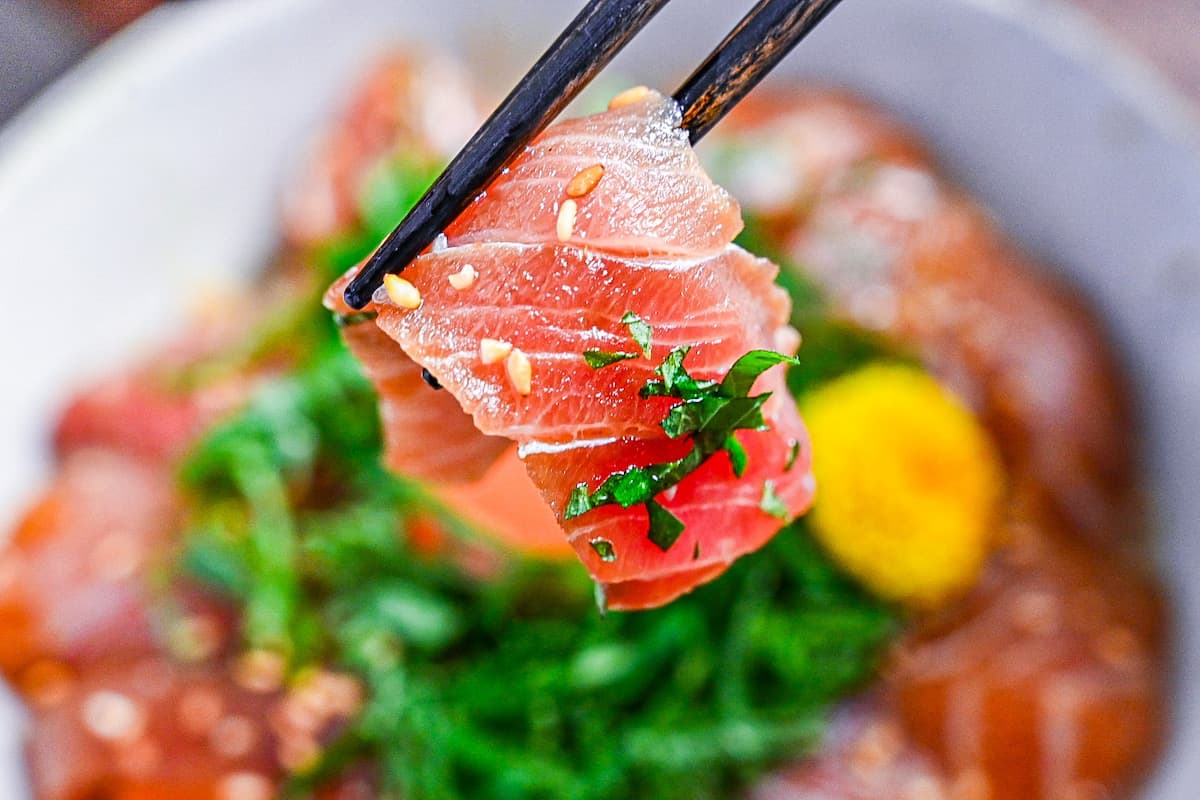 holding a piece of marinated tuna with black chopsticks