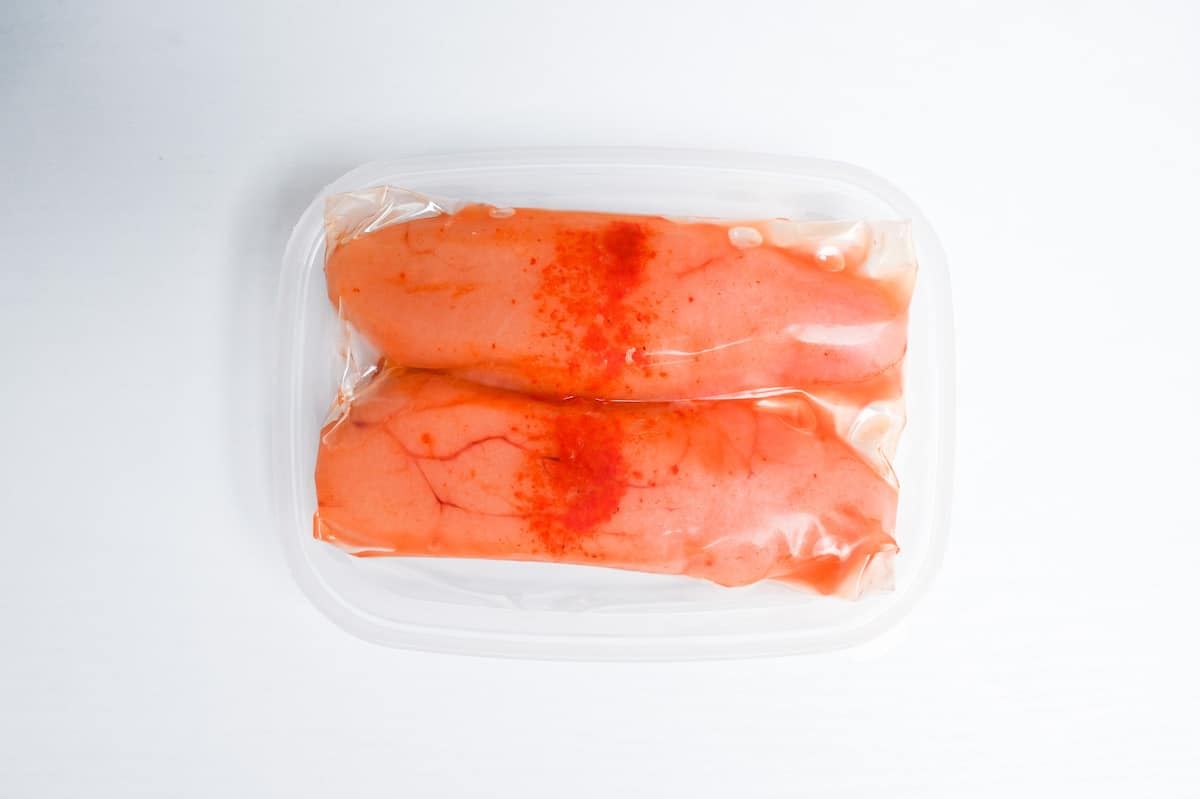 Two sacks of mentaiko with skins (spicy cod roe) in a plastic container