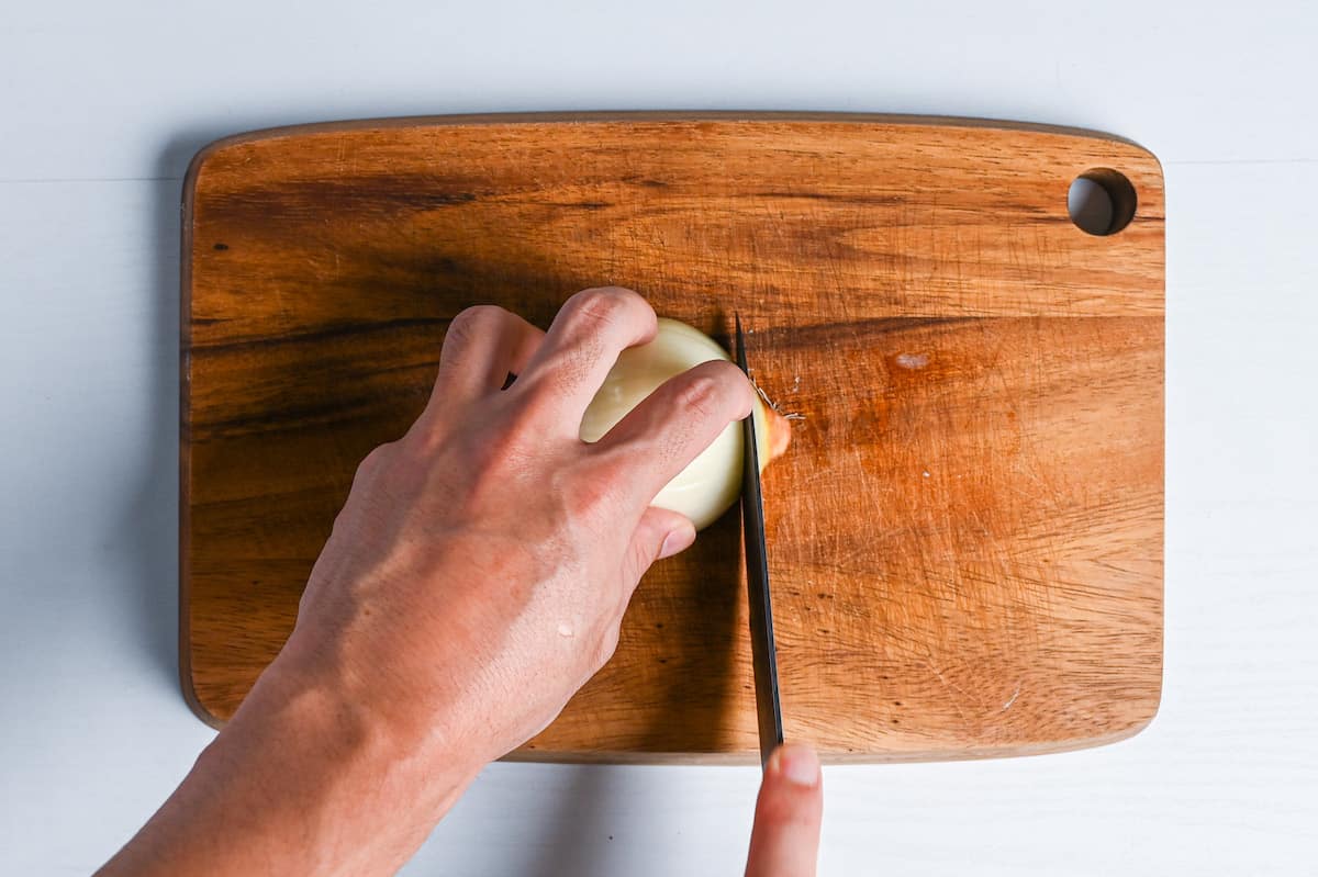 cutting end of onion on wooden chopping board