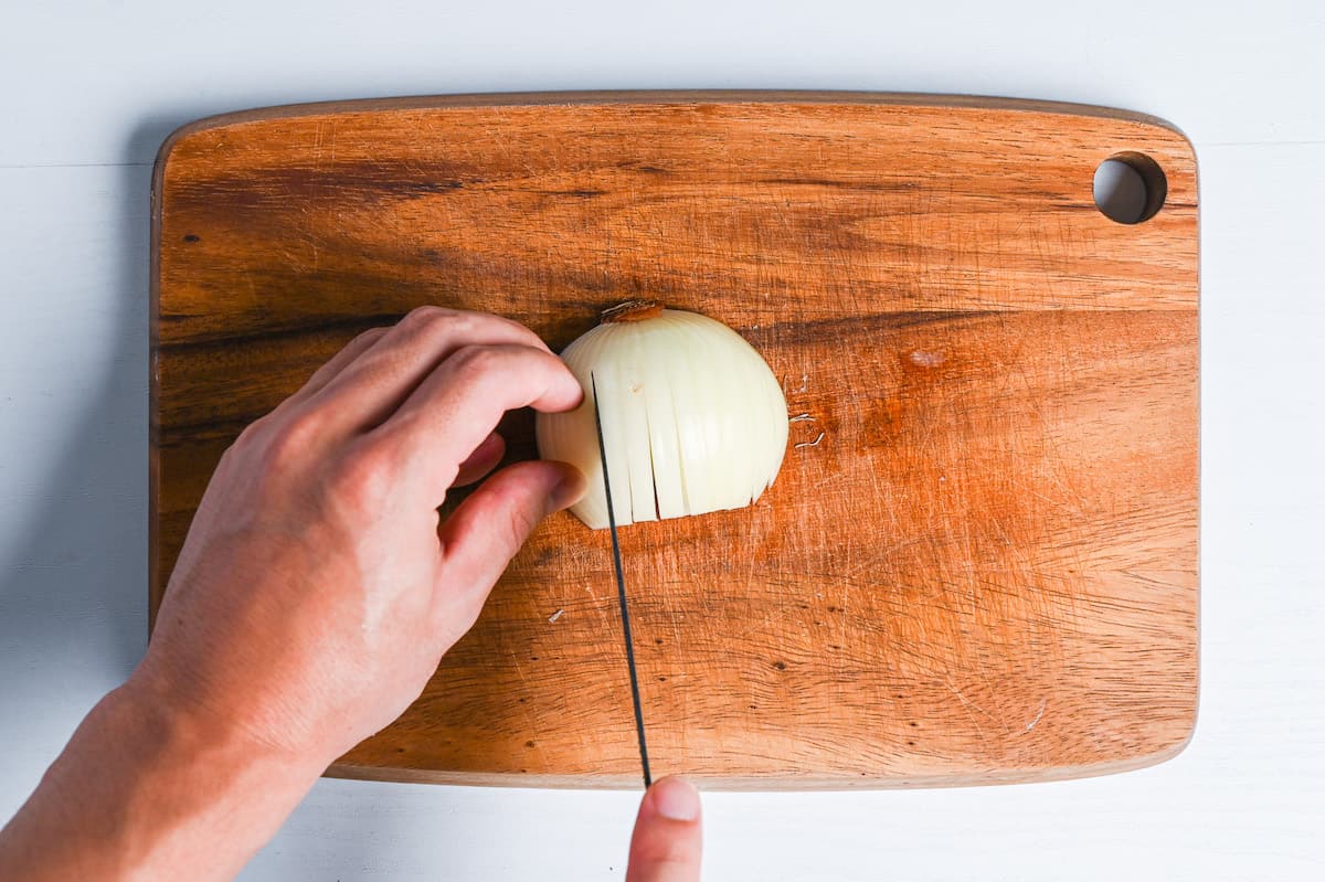 top-down of slicing onion on wooden chopping board
