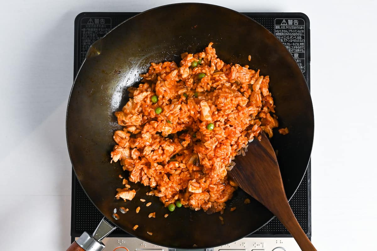 Ketchup fried rice with green peas and dried parsley in a wok