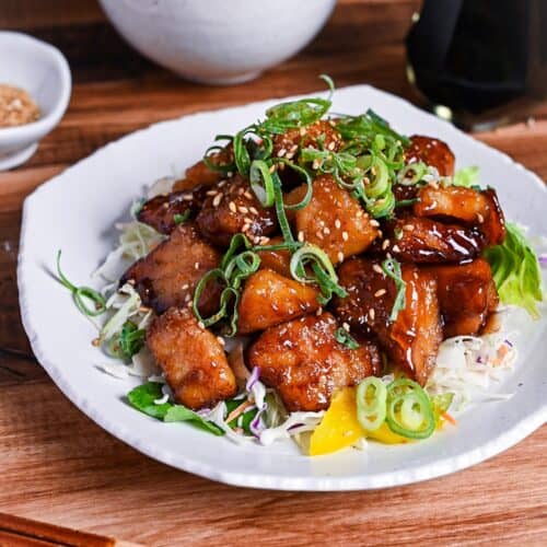 teriyaki cod served on a white plate over salad and topped with chopped green onion and toasted sesame seeds