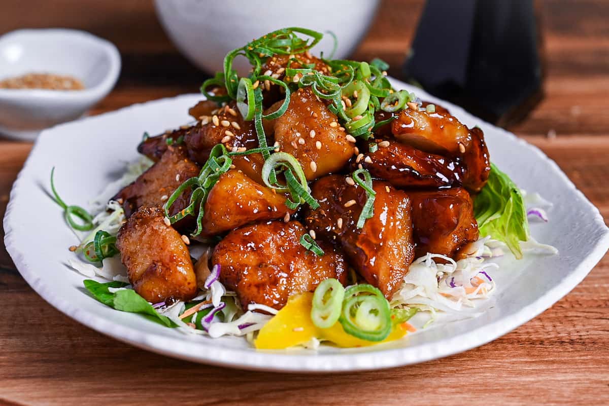 teriyaki cod served on a white plate over salad and topped with chopped green onion and toasted sesame seeds