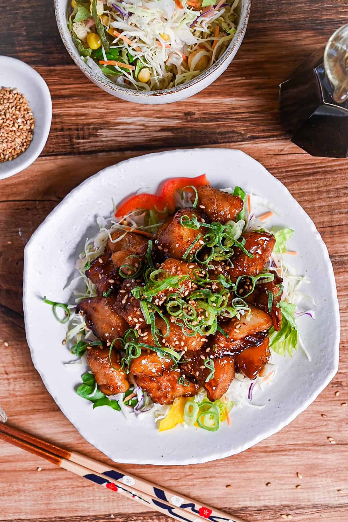 teriyaki cod served on a white plate over salad and topped with chopped green onion and toasted sesame seeds