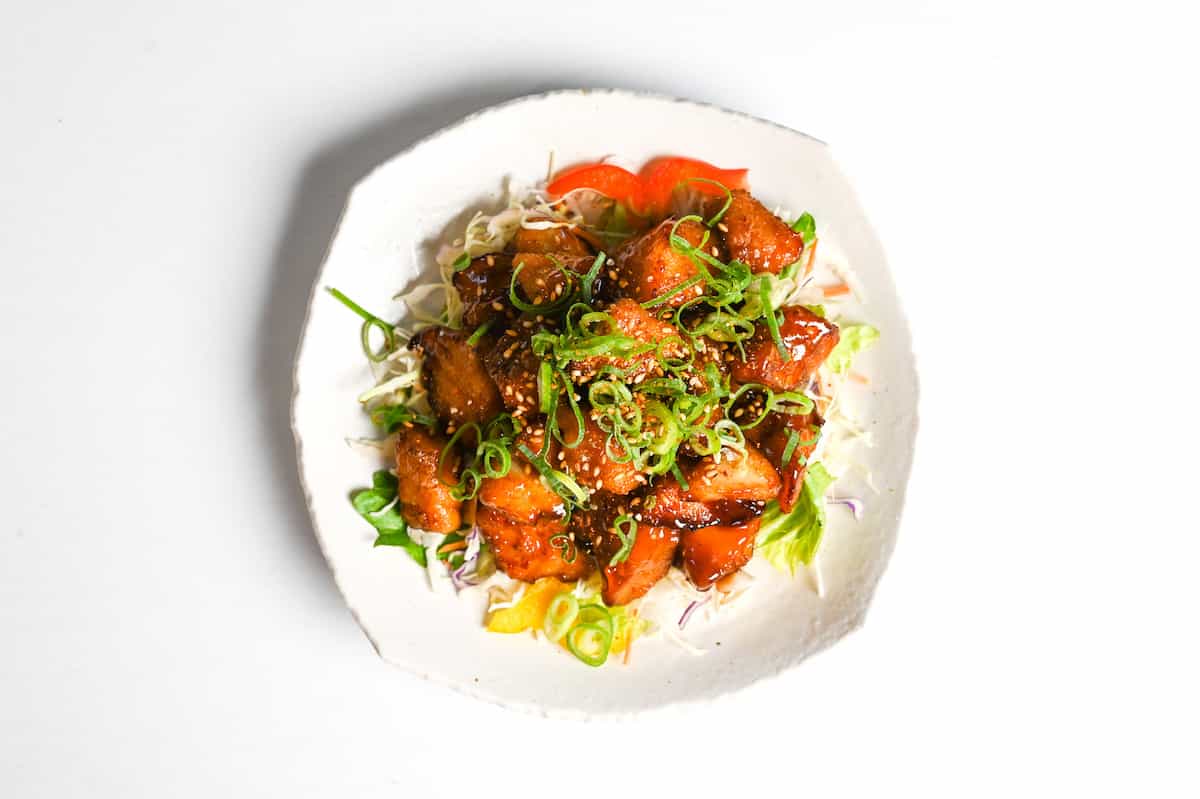 teriyaki cod served on a white plate over salad and topped with chopped green onion and toasted sesame seeds