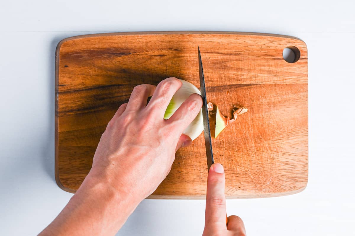 cutting end off half an onion on a wooden chopping board