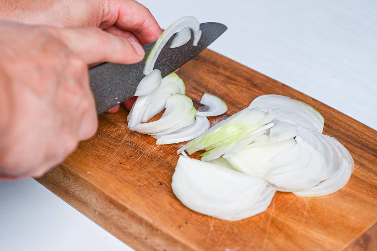 thinly slicing onion on wooden chopping board side view
