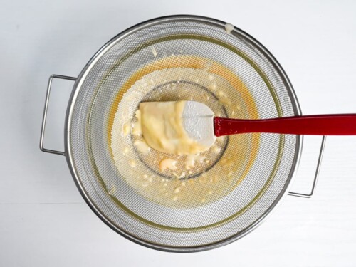 Mesh sieve placed over a large mixing bowl with the cheesecake mixture poured through