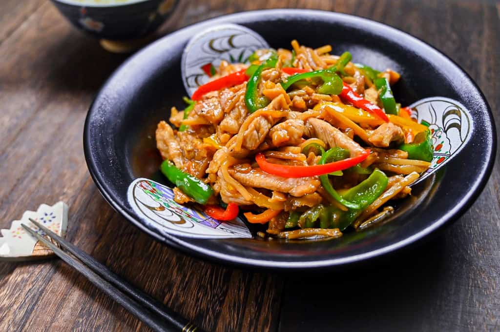 Chinjao Rosu Japanese pork and pepper stir fry served on a black plate with chopsticks on a fan shaped rest