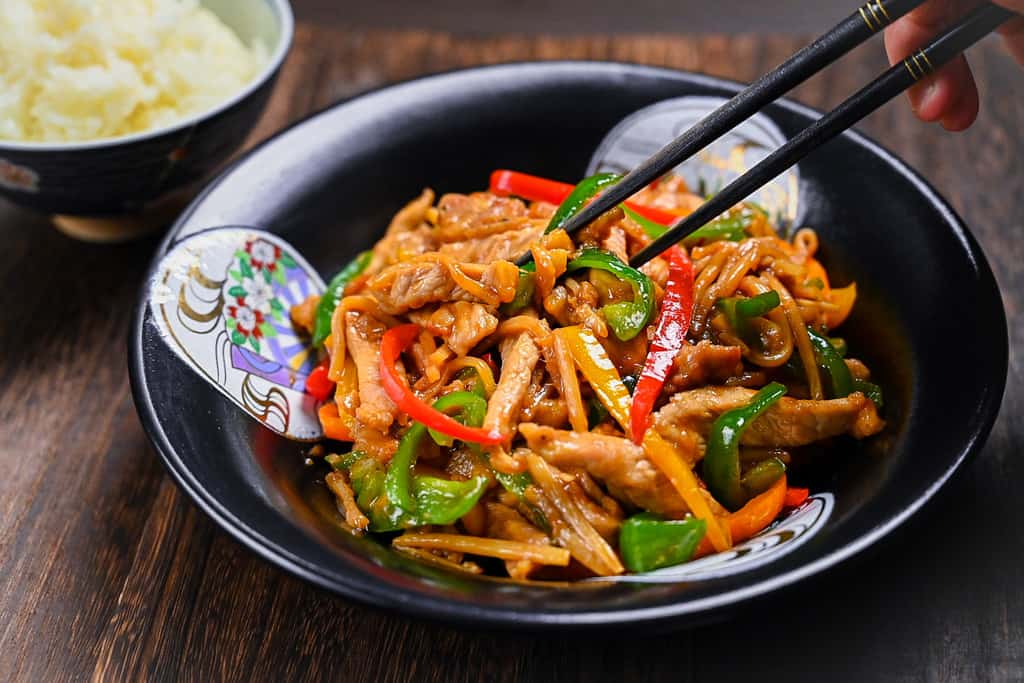 Chinjao Rosu Japanese pork and pepper stir fry served on a black plate with chopsticks