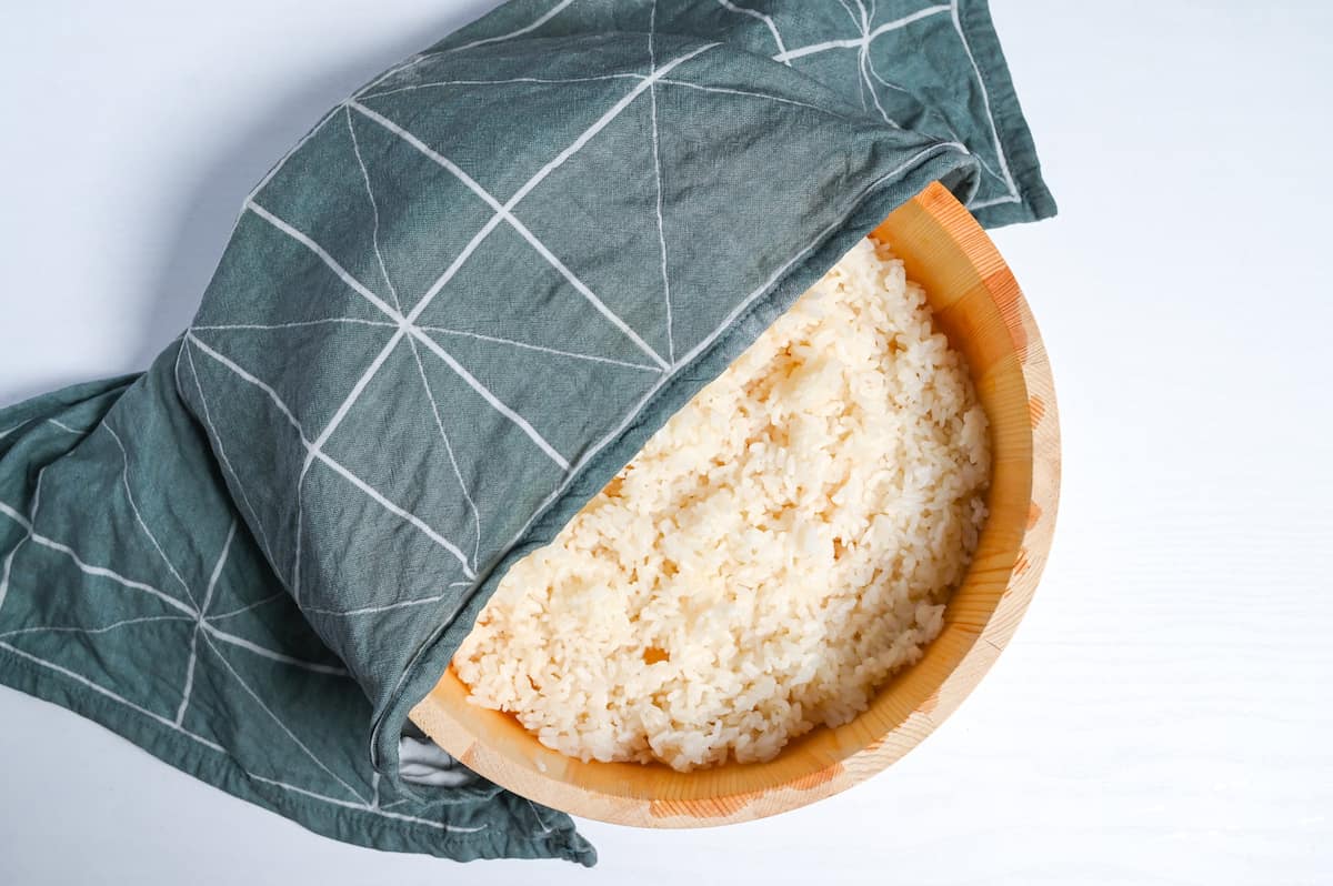 Japanese sushi rice in a wooden sushi-oke half covered with a damp tea towel