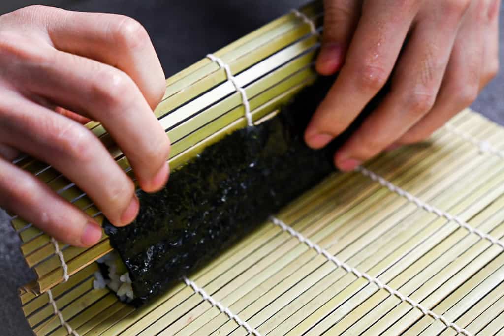 folding over the flap of nori using a bamboo rolling mat