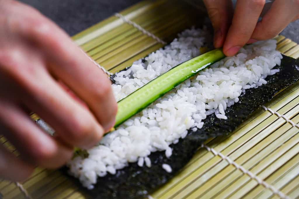 placing cucumber on sushi rice, making kappa maki
