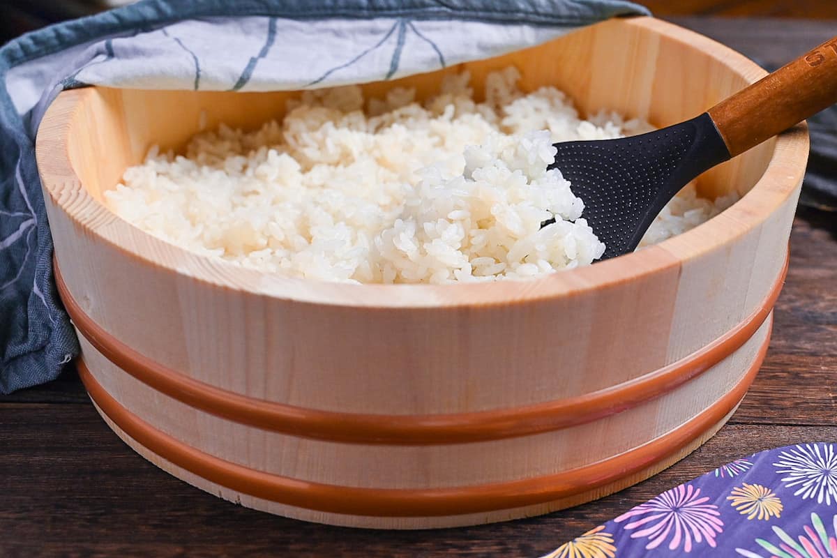 Japanese sushi rice in a sushi oke half covered with a teal tea towel side view