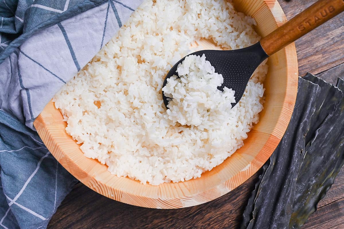 Japanese sushi rice in a sushi oke half covered with a teal tea towel