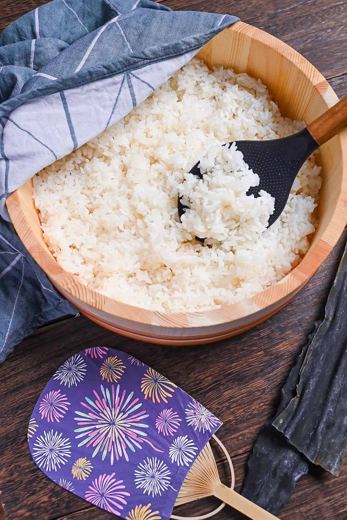 Japanese sushi rice in a sushi oke half covered with a teal tea towel