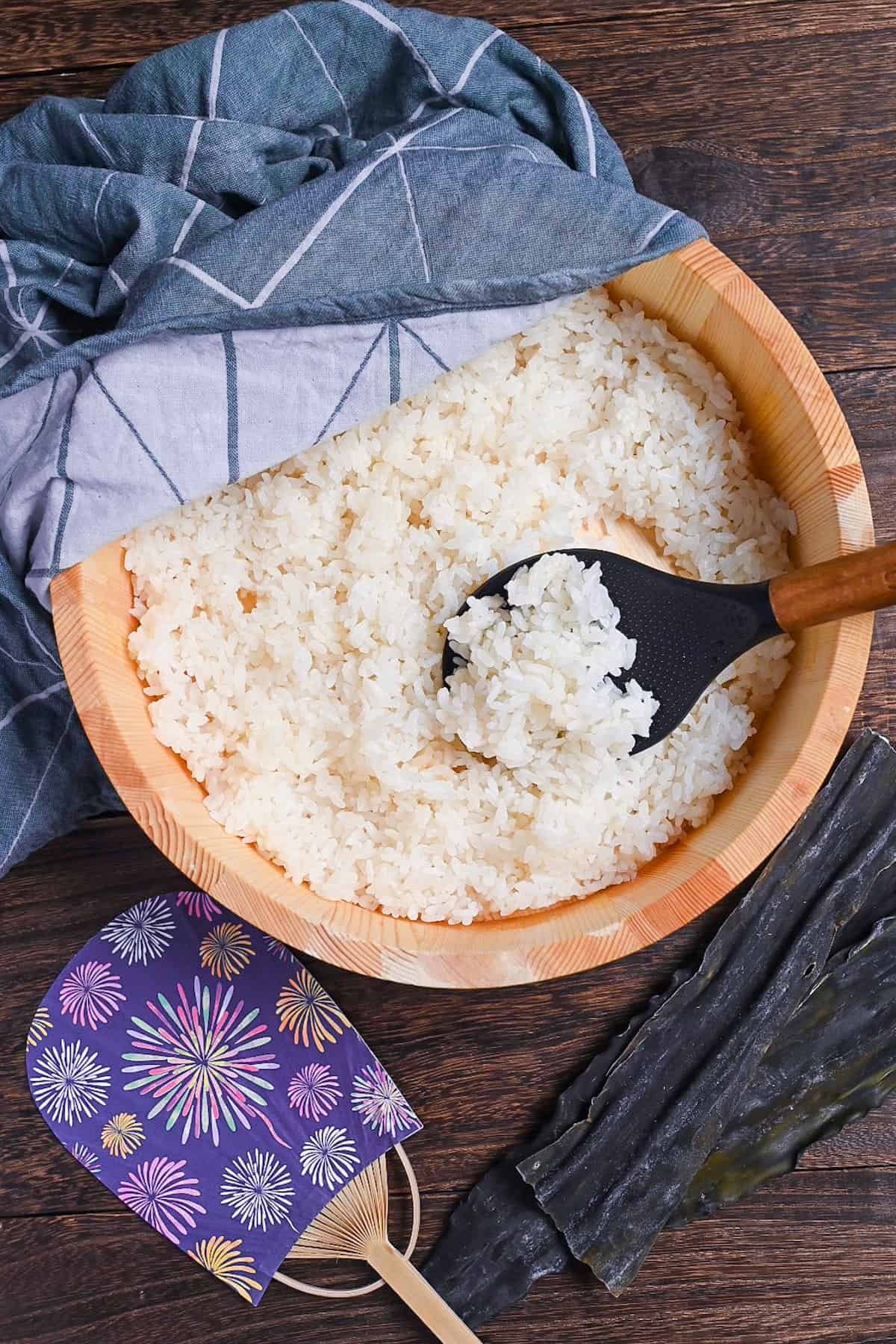 Japanese sushi rice in a sushi oke half covered with a teal tea towel top down