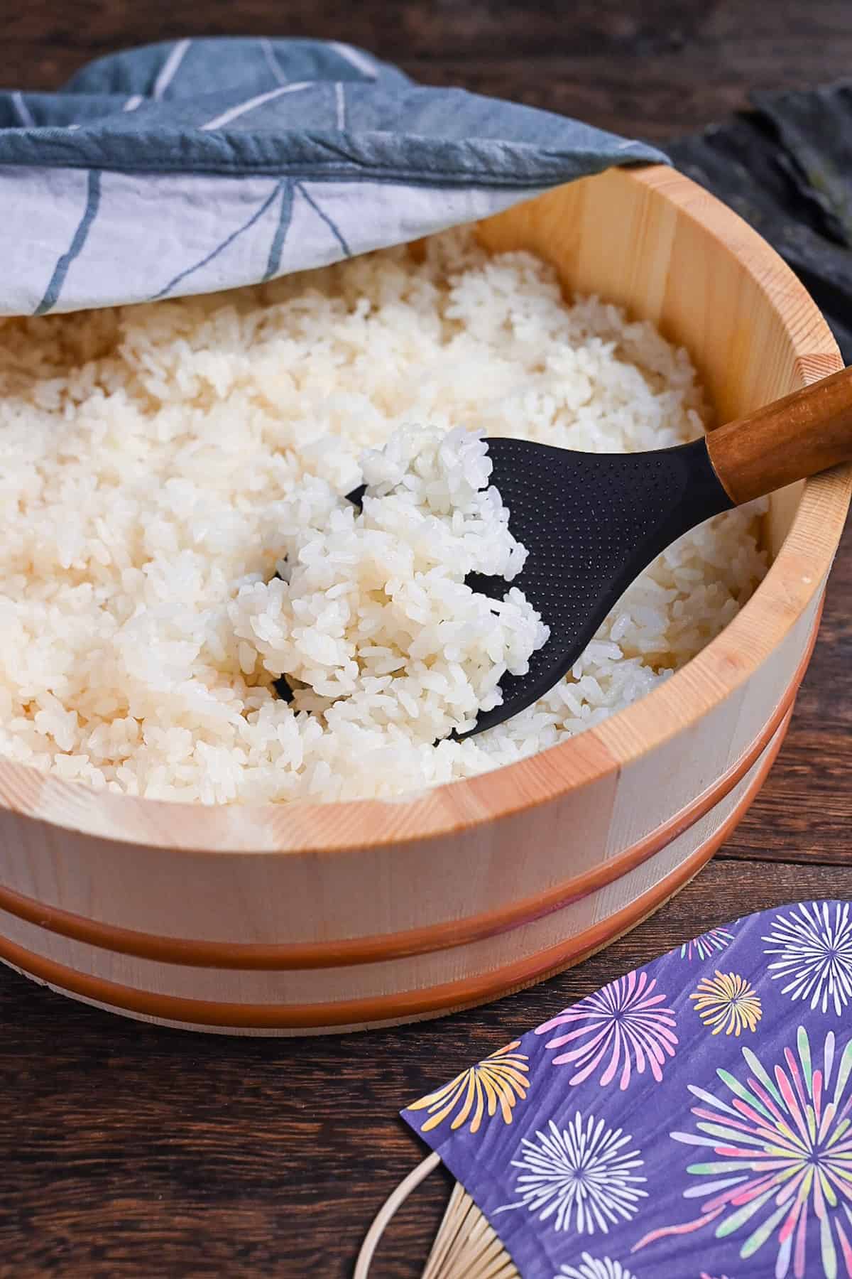 Japanese sushi rice in a sushi oke half covered with a teal tea towel