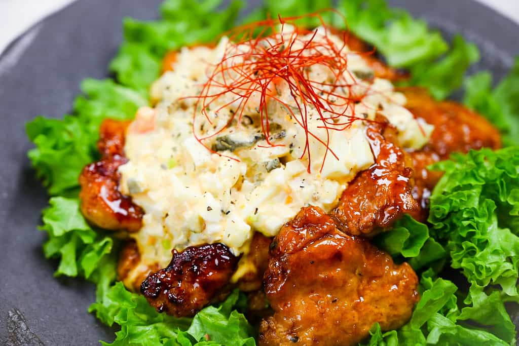 Japanese chicken nanban served on a bed of frilly lettuce on a black plate close up