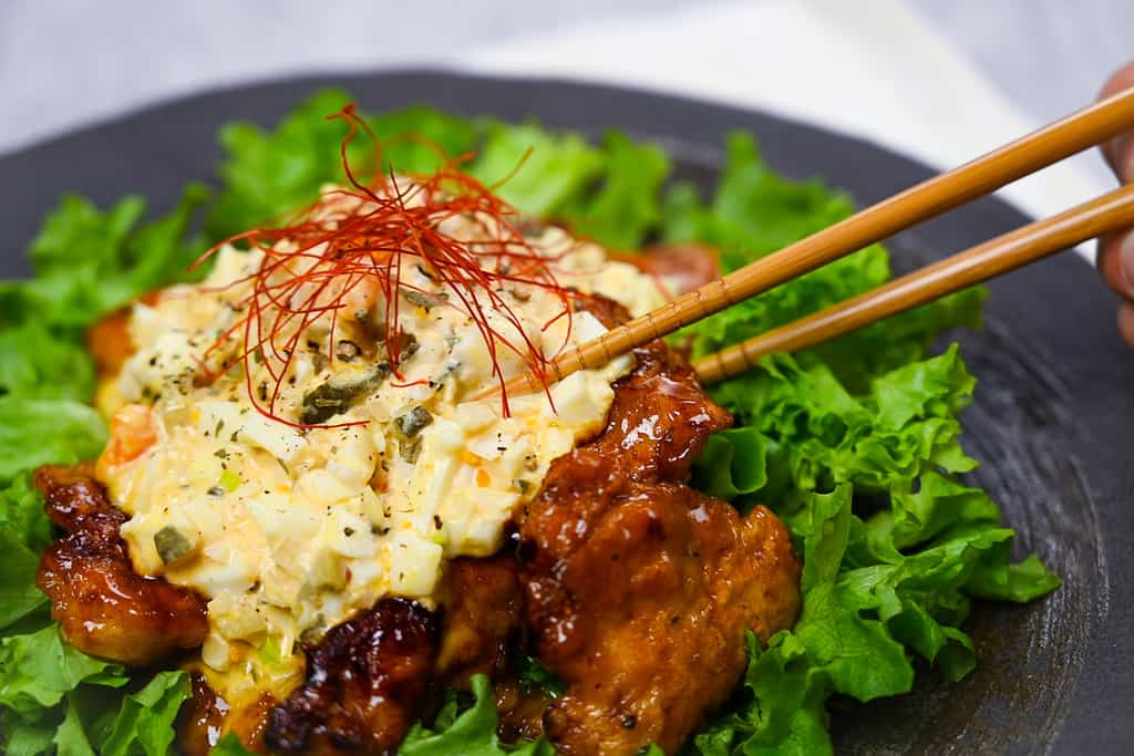 A piece of chicken nanban with tartar sauce picked up with wooden chopsticks