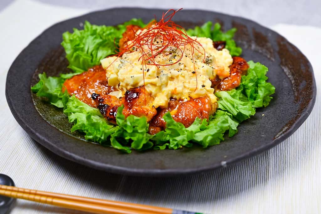 Japanese chicken nanban served on a bed of frilly lettuce on a black plate side view