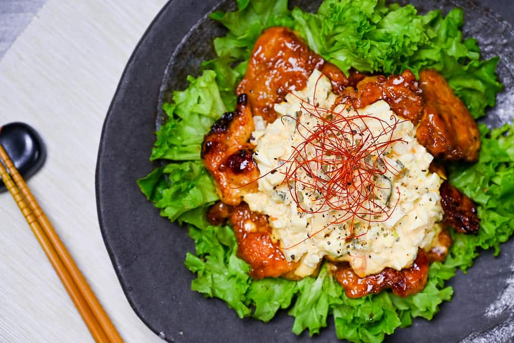 Japanese chicken nanban served on a bed of frilly lettuce on a black plate top down view