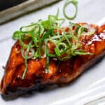 Teriyaki salmon served on a white fish plate garnished with spring onion