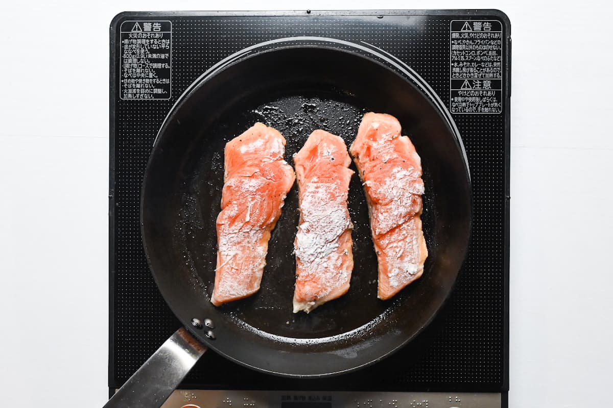 3 salmon fillets frying in a pan skin side down