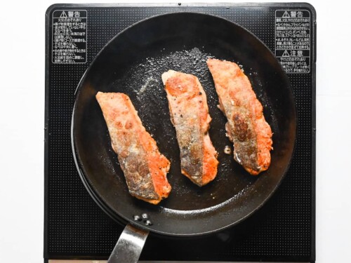 3 salmon fillets frying in a pan with skin side up