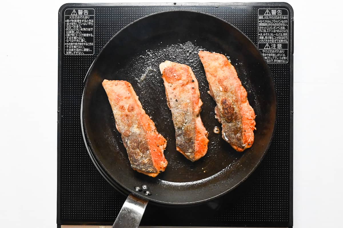 3 salmon fillets frying in a pan with skin side up
