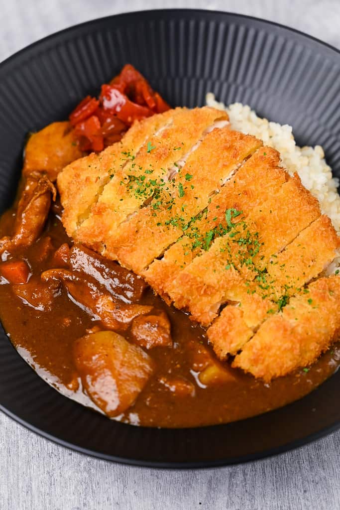 Chicken katsu curry with rice and pickles on a black plate