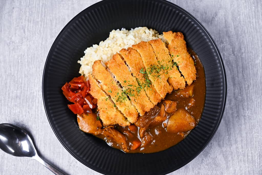 Chicken katsu curry with rice and pickles on a black plate top down